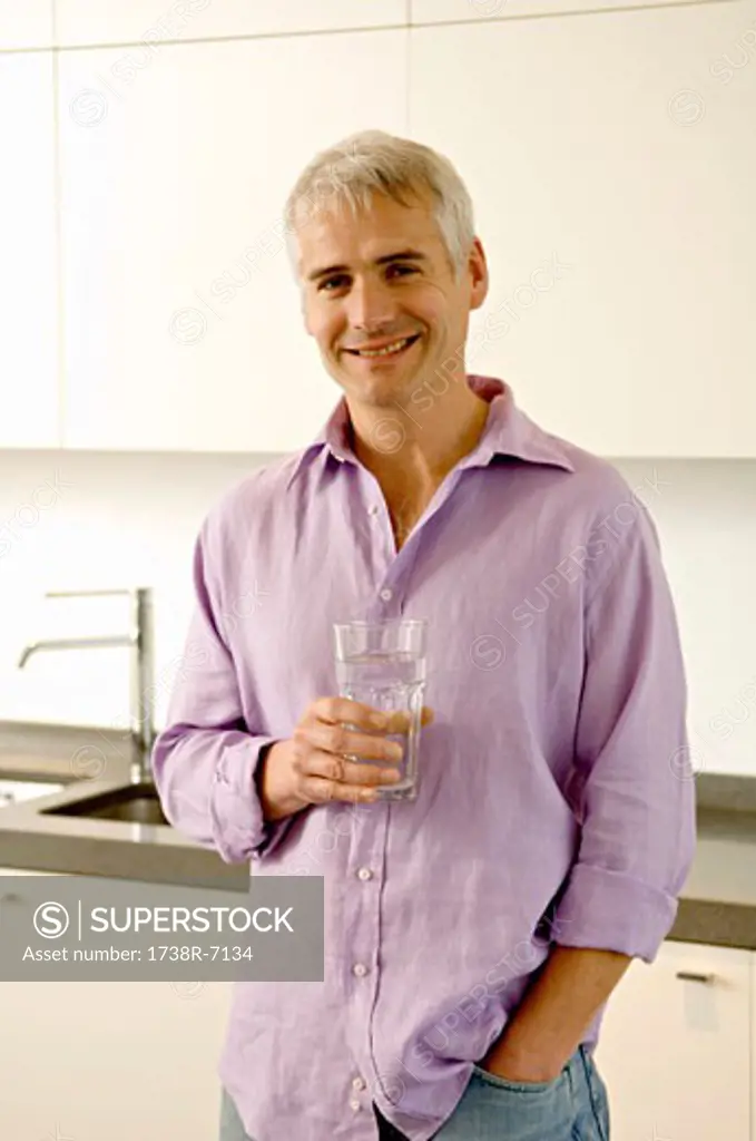 Portrait of a mature man holding a glass of water in the kitchen