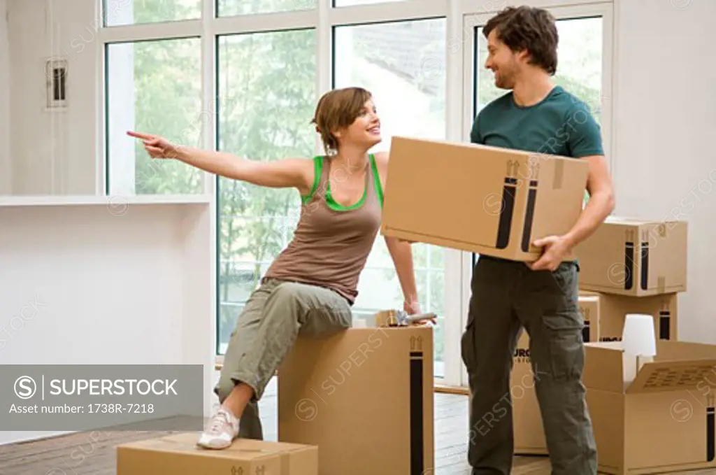 Mid adult man holding a cardboard box and a young woman pointing away