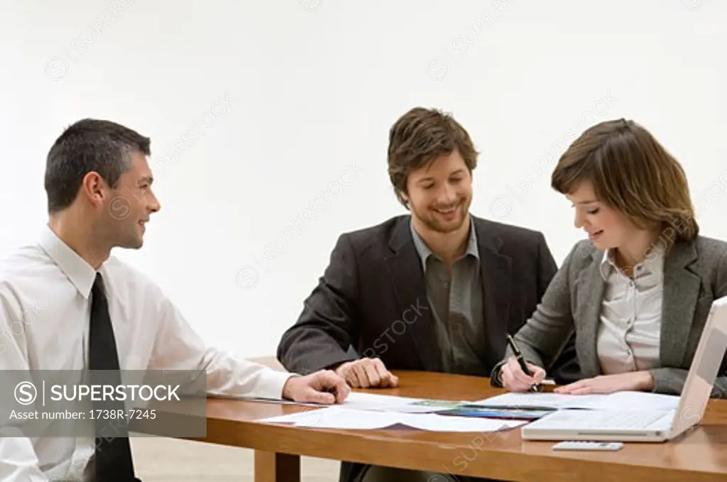 Young woman filling a document with a mid adult man and a real estate agent sitting with her