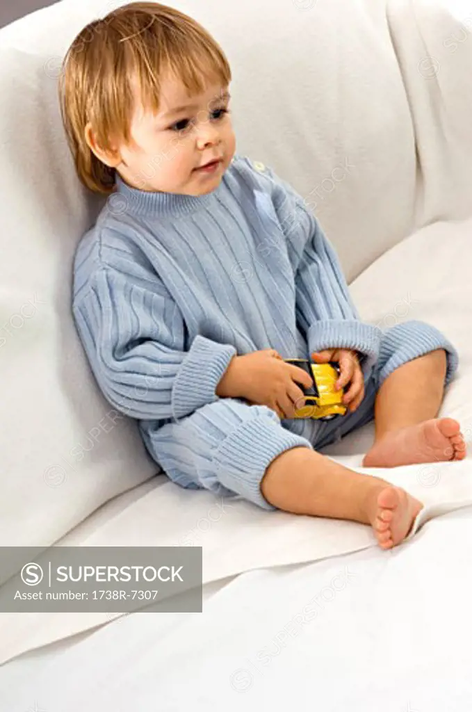 Baby boy sitting on a couch and holding a toy car