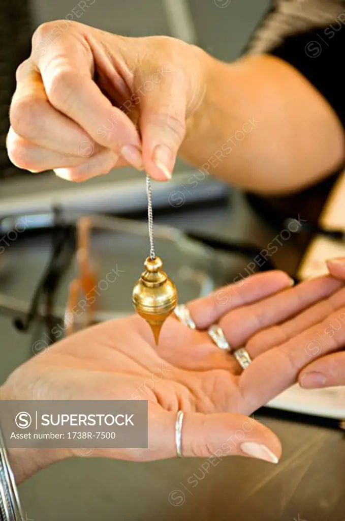 Close-up of a woman's hand holding a dowsing pendulum over a woman's palm