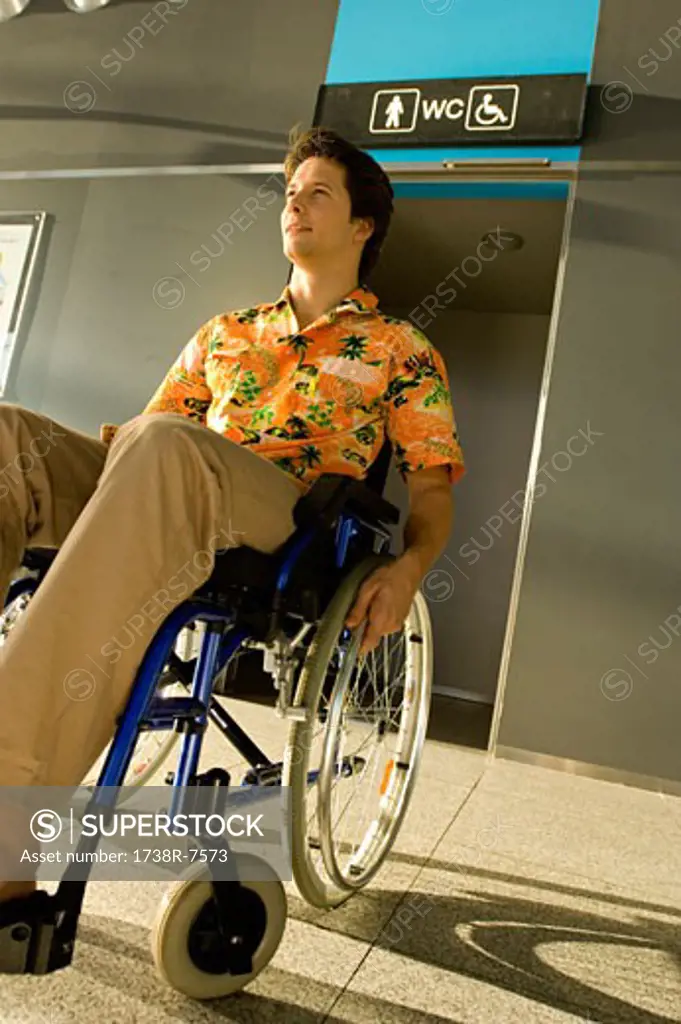 Mid adult man sitting in a wheelchair in front of a restroom entrance