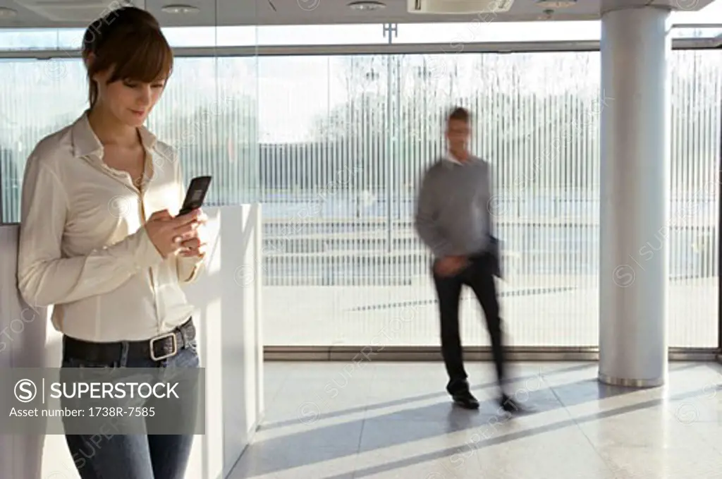 Businesswoman using a mobile phone with a businessman walking in the background