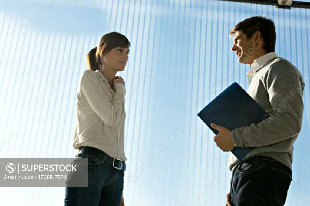 Side profile of a businessman holding a laptop and talking to a businesswoman