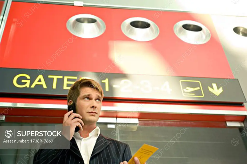 Low angle view of a businessman holding a boarding pass and talking on a mobile phone