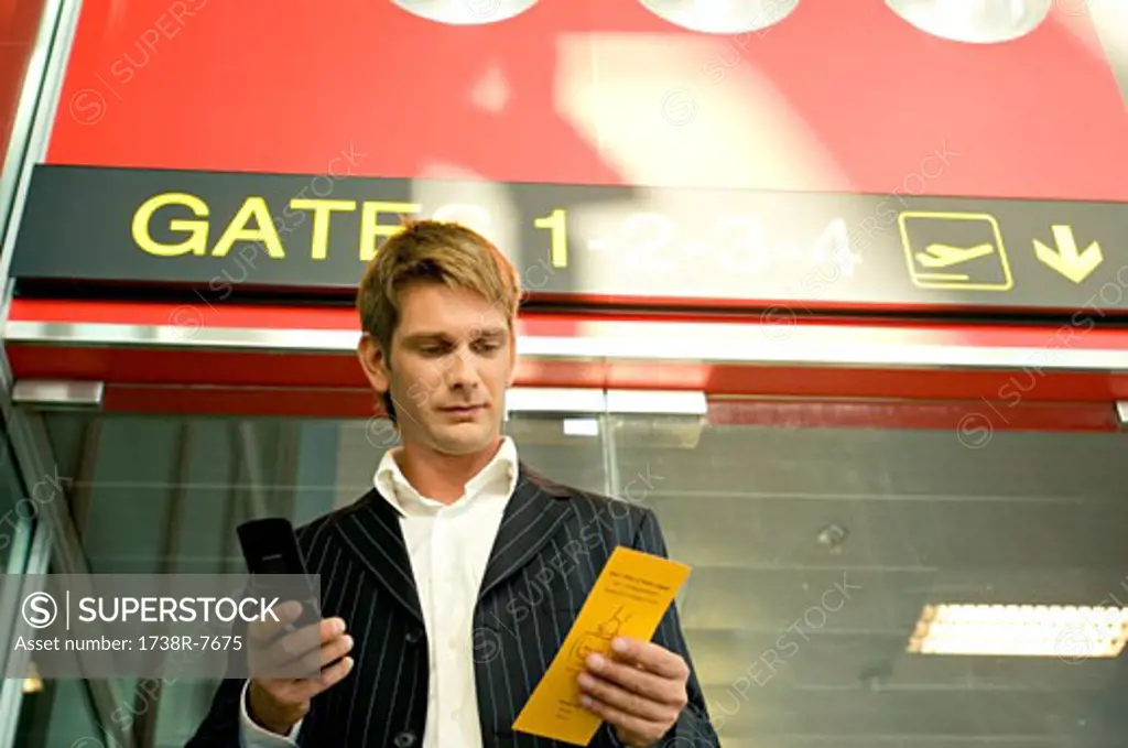 Low angle view of a businessman holding a boarding pass and using a mobile phone