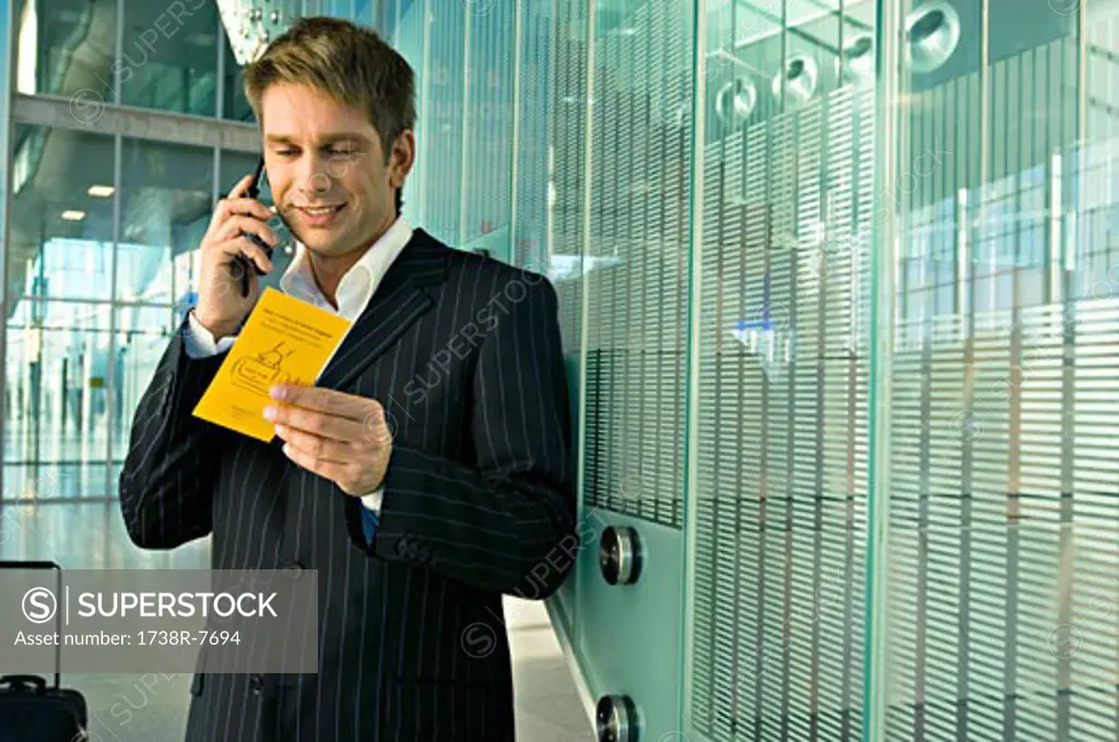 Businessman holding an airplane ticket and talking on a mobile phone at an airport