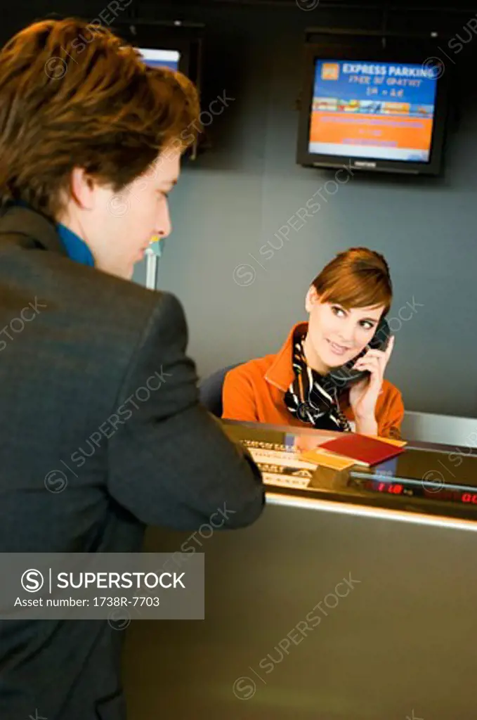 Businessman standing at an airport check-in counter while the check-in attendant talking on the telephone