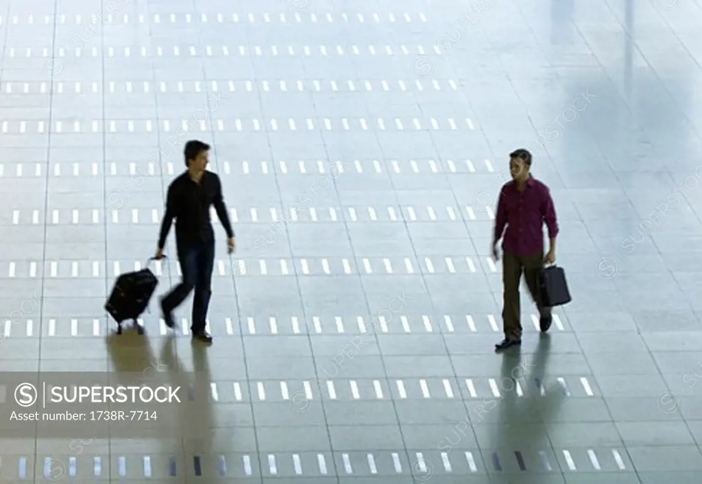 High angle view of a mid adult man and a young man walking at an airport lobby