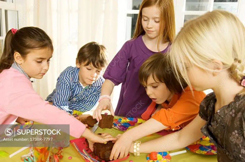 Children picking up pieces of a cake