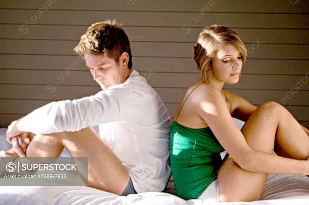 Side profile of a mid adult man and a young woman sitting back to back on the bed