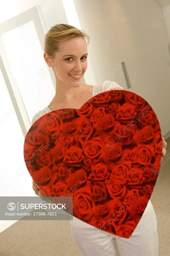 Young woman holding a heart shape gift and smiling