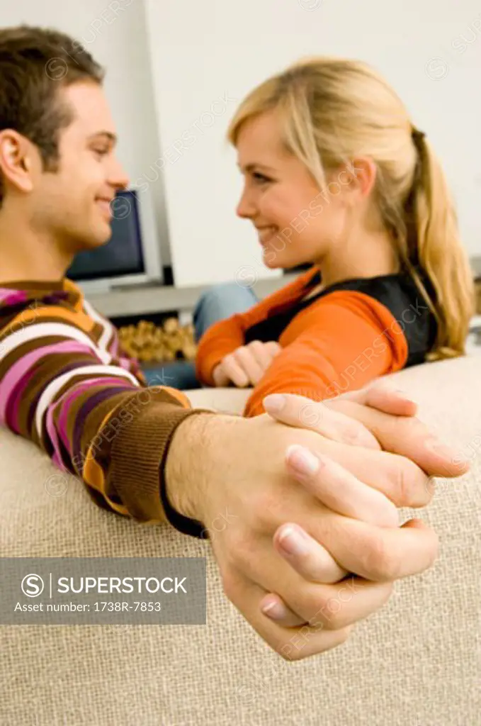 Side profile of a young couple sitting on a couch and holding each other's hands