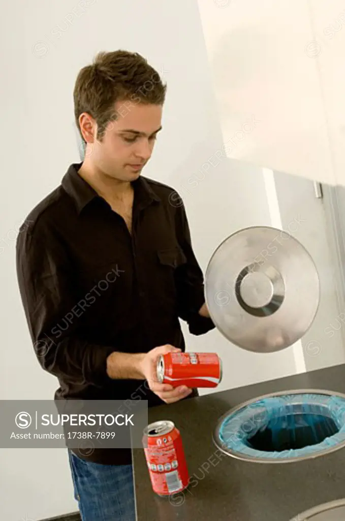 Young man putting a drink can in a garbage bin