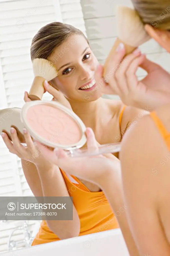Reflection of a young woman applying make-up on her face