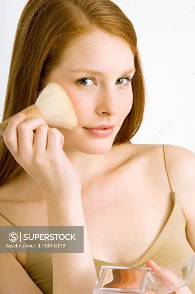 Portrait of a young woman applying blush on her cheek