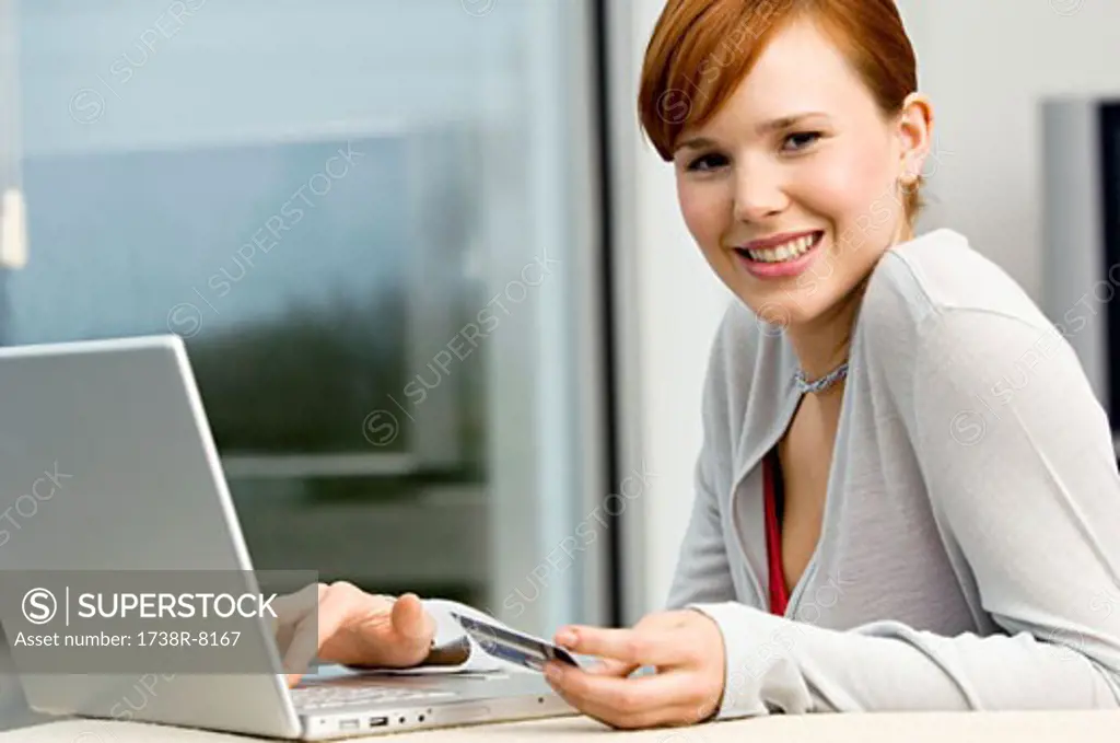 Portrait of a young woman holding a credit card and using a laptop