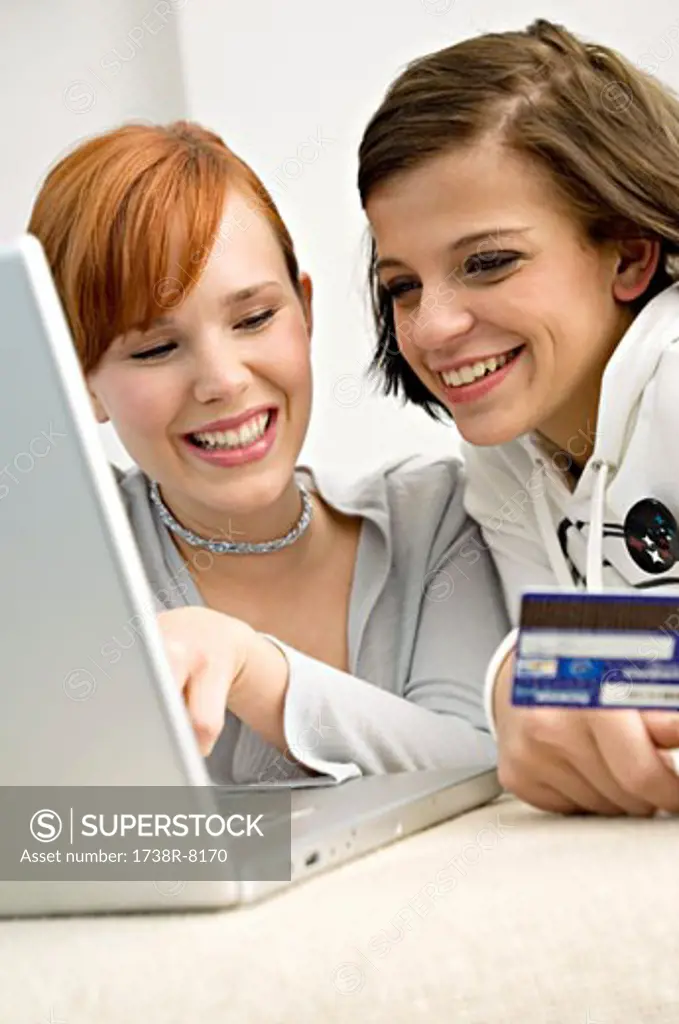 Close-up of two young women holding a credit card and using a laptop