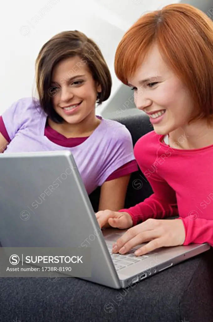 Two young women using a laptop and smiling