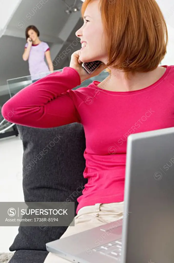 Young woman using a laptop and talking on a mobile phone