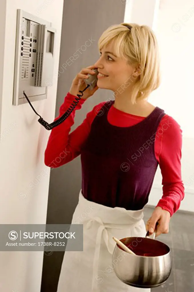 Young woman holding a saucepan and talking on the telephone