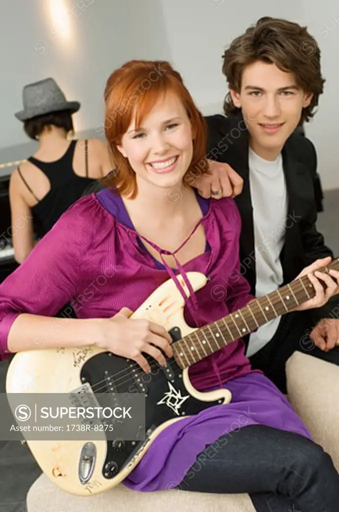 Portrait of a young woman playing a guitar with a teenage boy sitting beside her