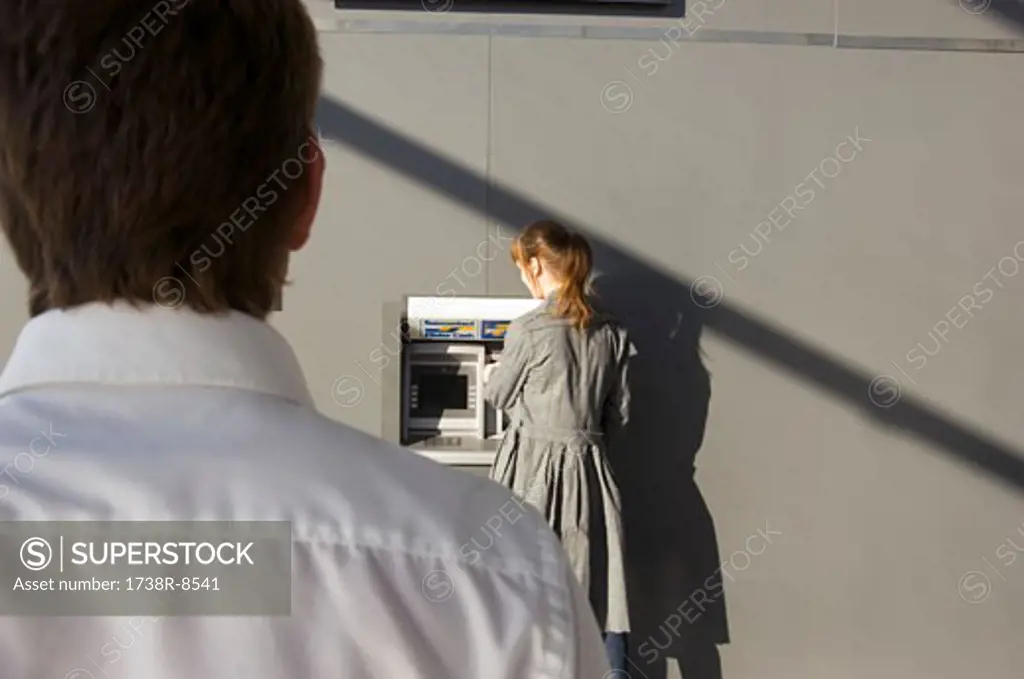 Rear view of a businessman looking at a businesswoman using an ATM