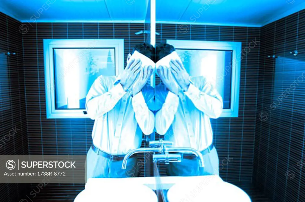 Man covering face while leaning by mirror in washroom