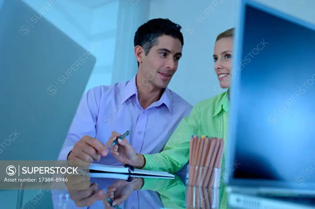 Businessman sitting with female colleague in office, smiling