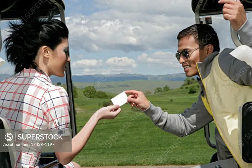Man passing a woman a card from a golf cart