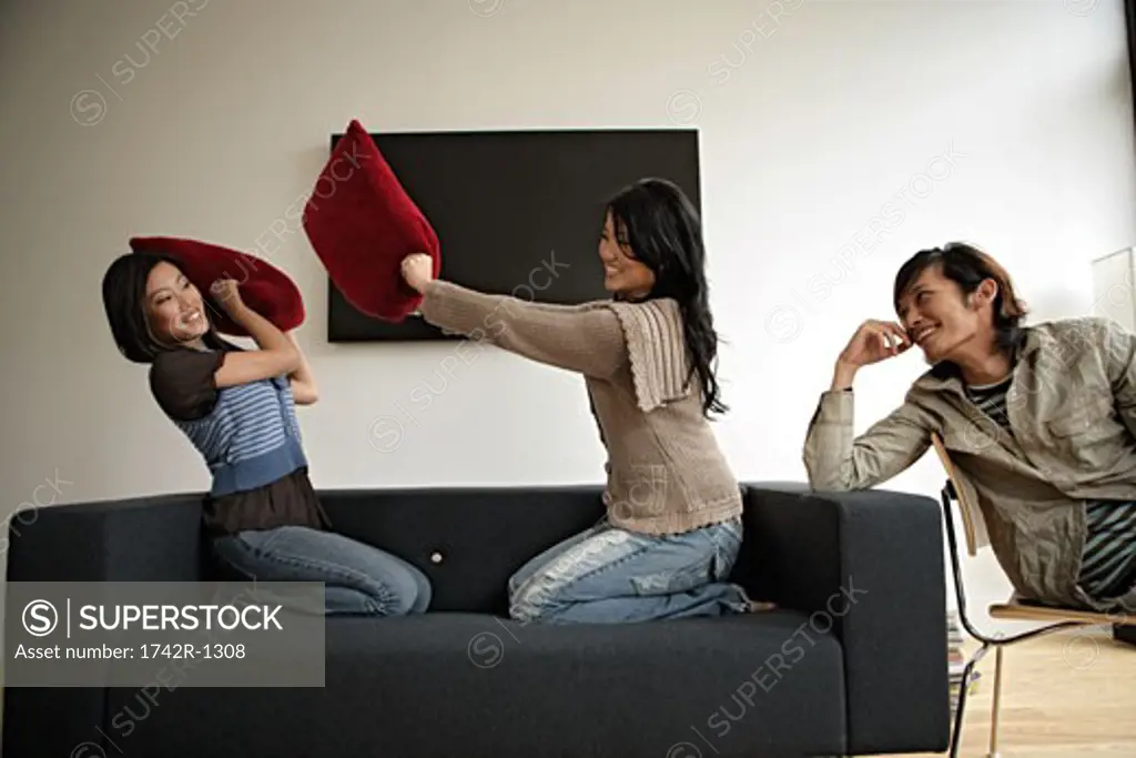 Two women fighting with pillows while man observing, side view