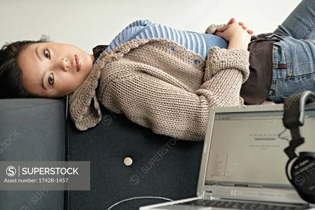 Young woman lying on sofa with headphone and laptop, side view