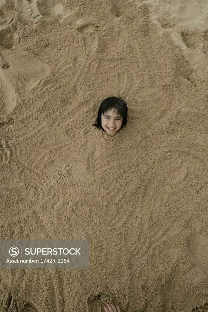 A small girl is buried in sand.