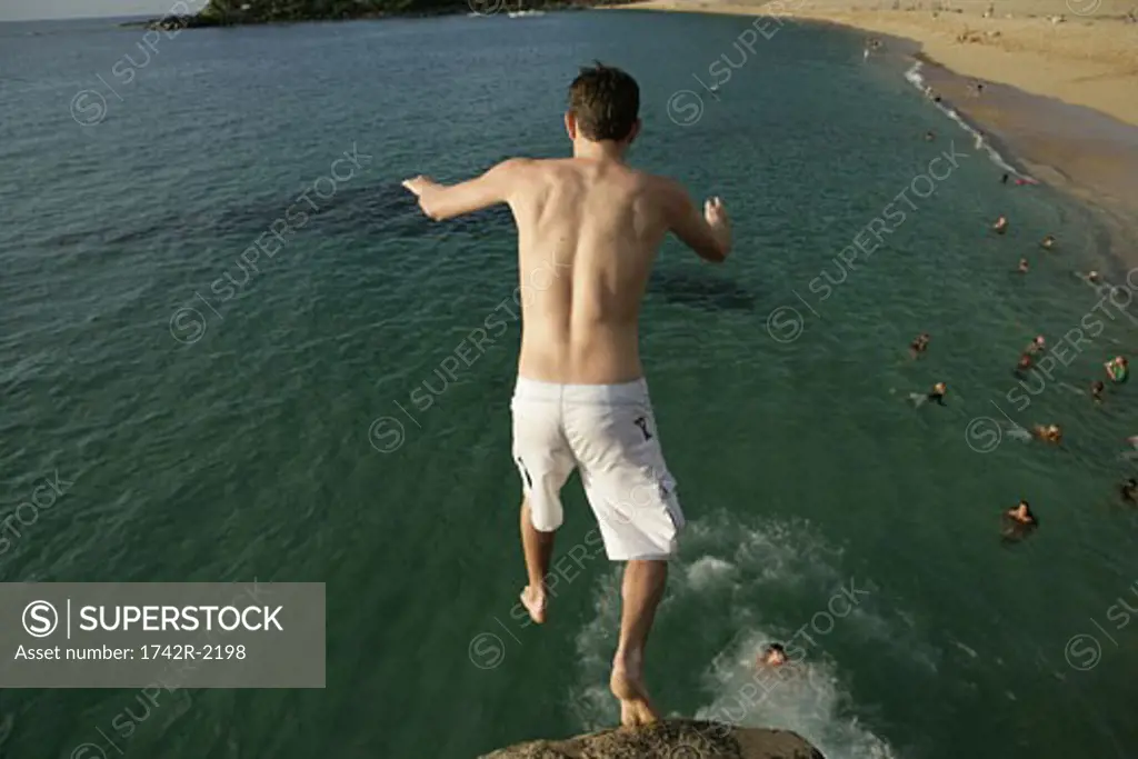 A man is jumping off a cliff into the sea.