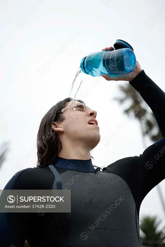A young man is pouring water on himself.