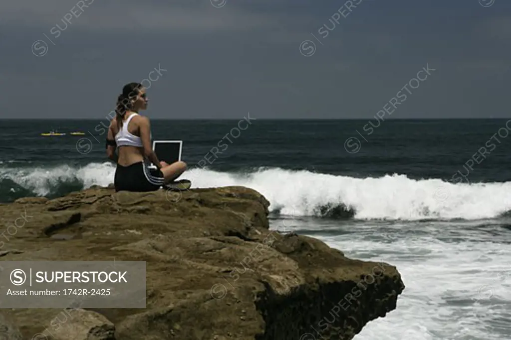 View of a woman working on a laptop near a sea.