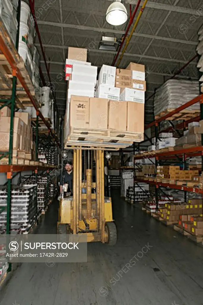 View of a worker driving a forklift inside a warehouse.