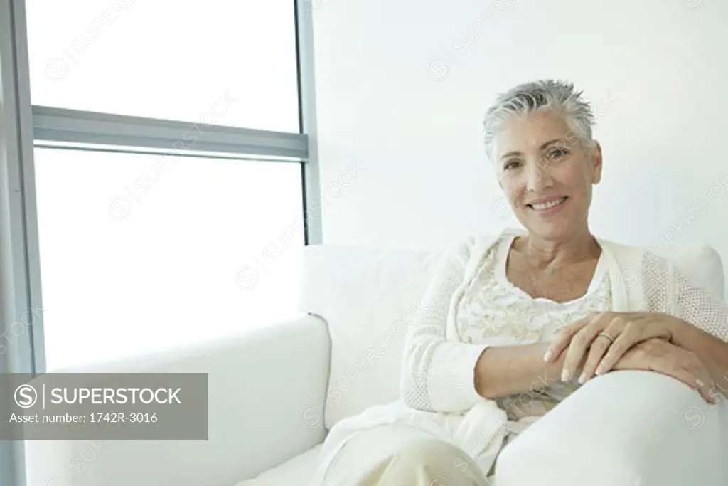 Mature woman sitting with her legs crossed in a white chair