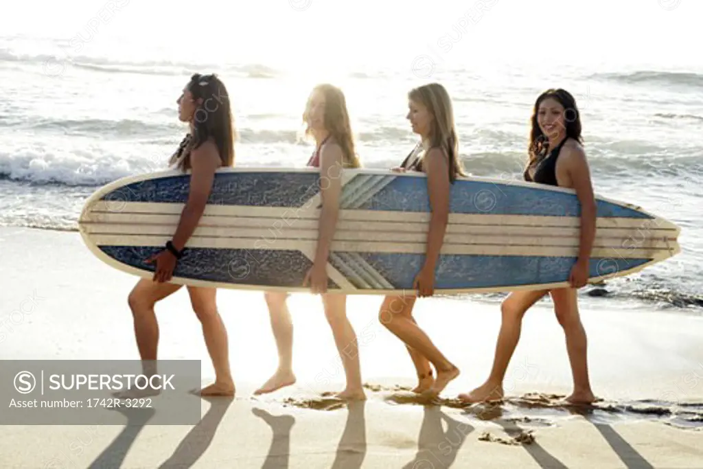 View of four young women carrying a surfboard.