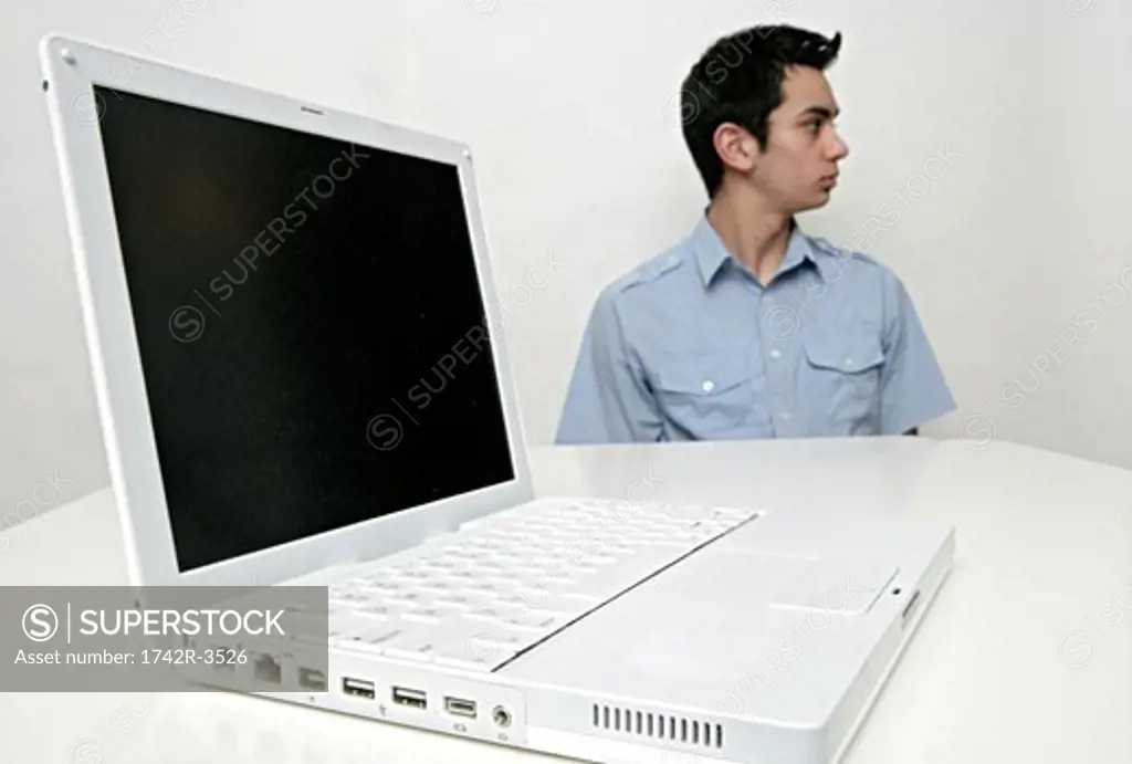 View of a teenage boy and a laptop on a table.