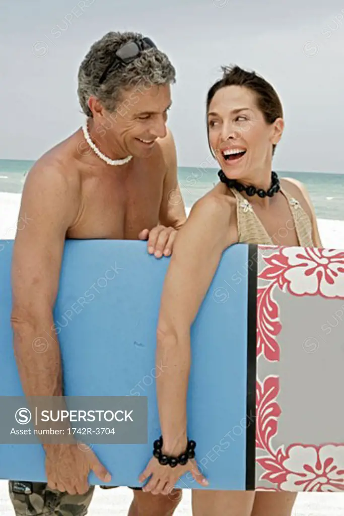 Couple carrying a surfboard on beach.