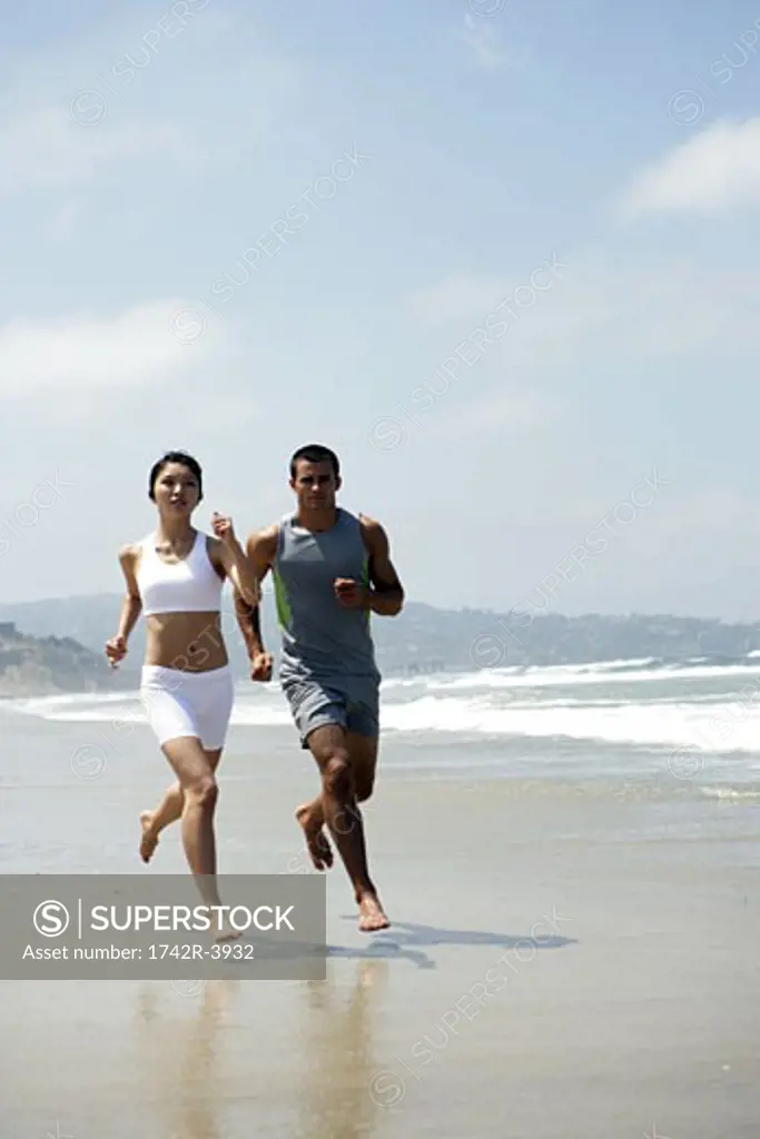 A couple are jogging together on a beach.