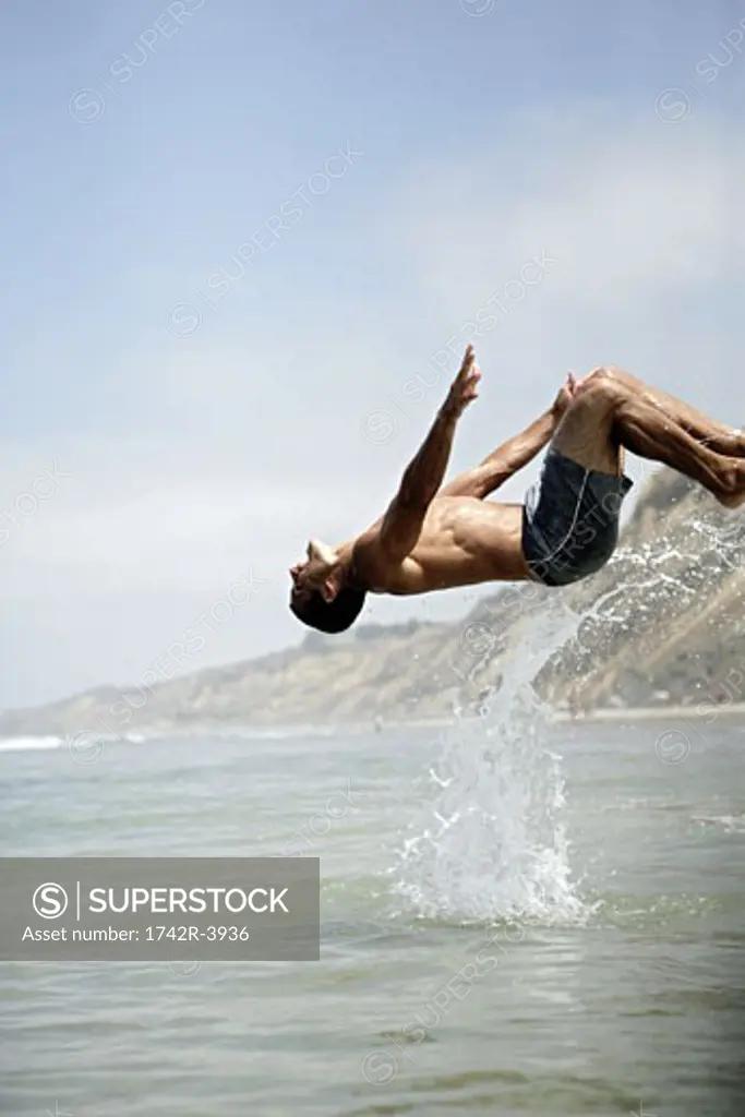 A man dives backward into the sea.