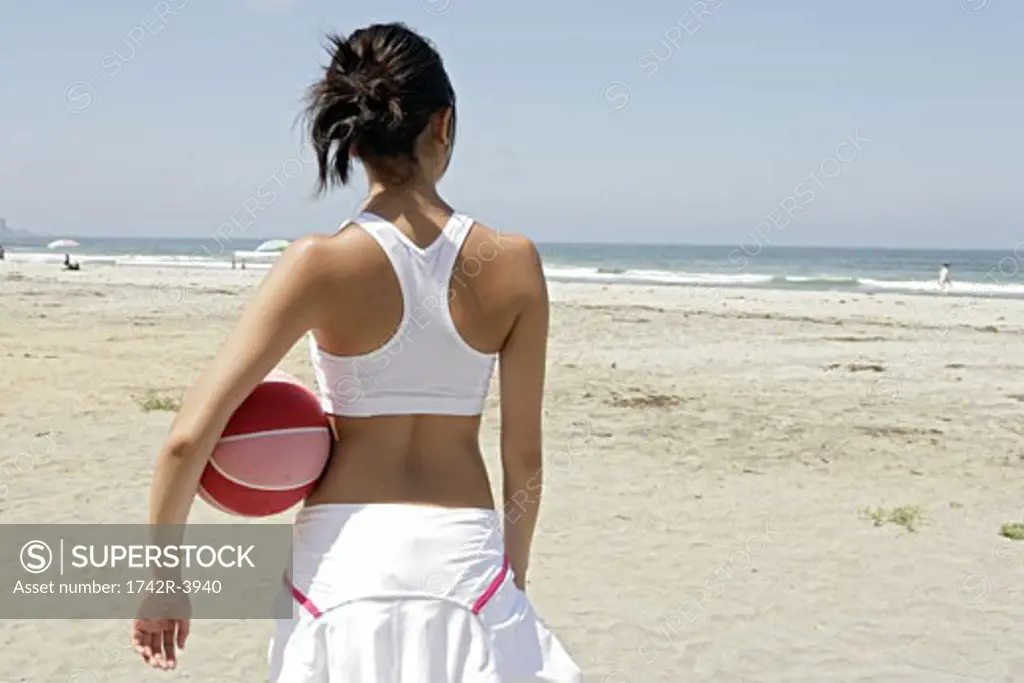 A woman is holding a rubber ball and standing on a beach.