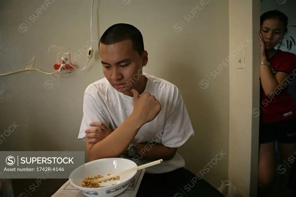 Teenage boy (15-17) sitting in front of bowl with chopsticks and newspaper