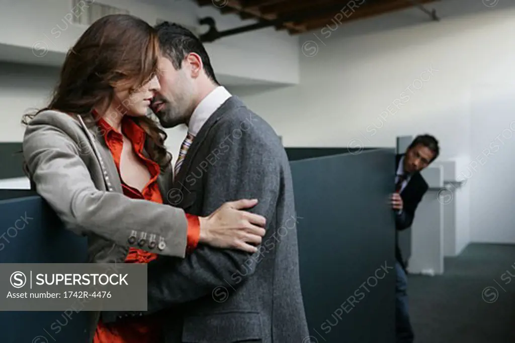 Man peeking at couple embracing in the office