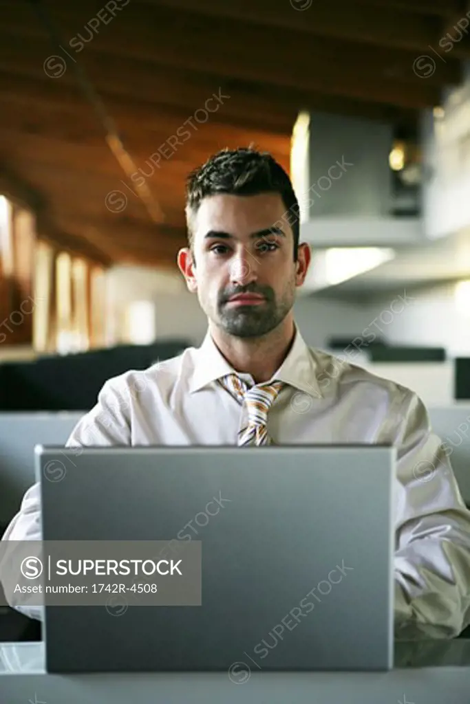 Businessman seated at a laptop computer, looking at camera