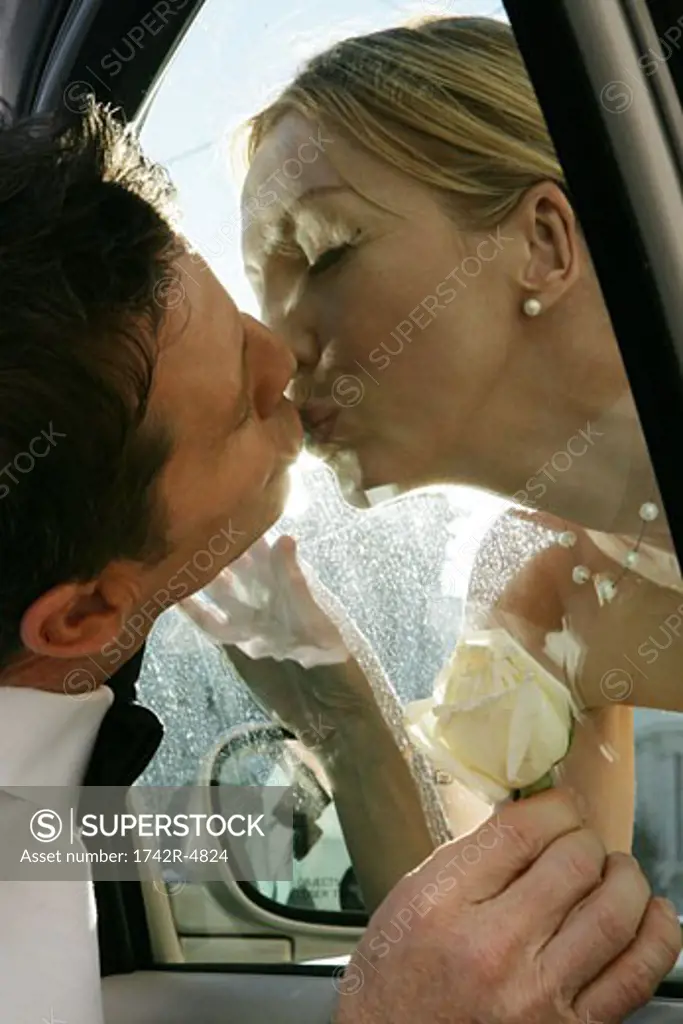 Mature couple kissing each other through the window of a car