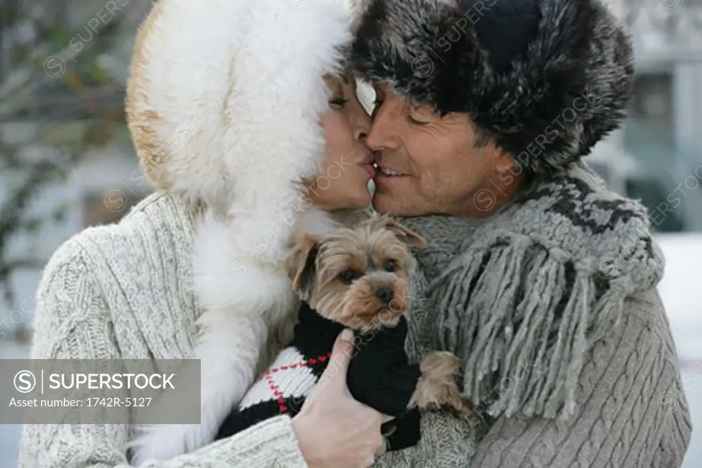 Mature couple kissing while holding a Yorkshire Terrier