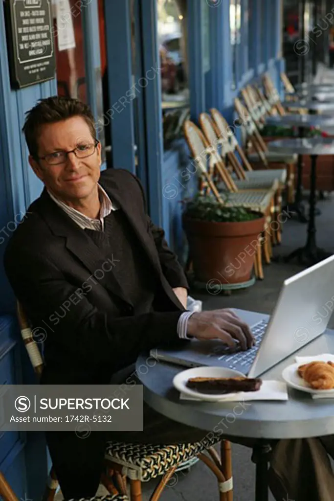 Mature man typing on a laptop at a cafe
